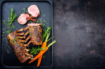 Barbecue rack of lamb with carrot and herbs offered as top view on a modern design cast iron tray...