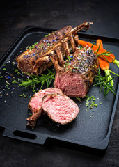 Barbecue rack of lamb with carrot and herbs offered as closeup on a modern design cast iron tray