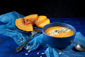 pumpkin cream soup in a blue plate on a deep classic blue background with slices of pumpkin with blue gauze and a spoon.