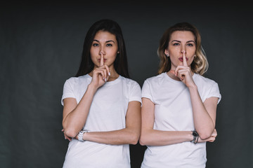Secretive ladies keeping silence standing in studio