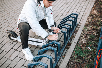 man hangs a cable lock on an electric scooter in a bicycle parking lot. Protection against theft of vehicles.