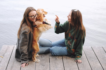 Two girls and english cocker spaniel dog lying on wooden bridge.Portrait of dog outside (outdoors)....