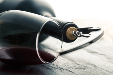 Stainless corkscrew in a cork of bottle neck and wine glass with wine lying on a black slate...