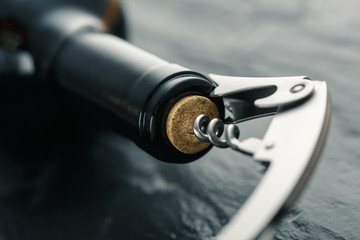 Stainless  wine corkscrew in a cork of wine bottle neck on a black slate background