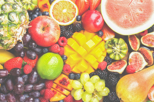 Healthy raw rainbow fruit background, mango papaya strawberries oranges blueberries pineapple watermelon obn wooden board on light concrete background, top view, selective focus
