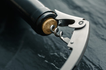 Stainless  wine corkscrew in a cork of wine bottle neck on a black slate background