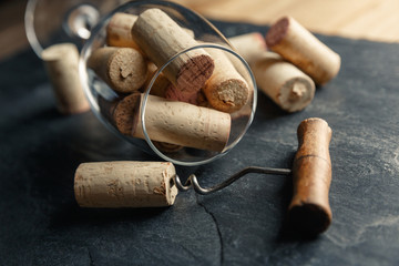 Fototapeta na wymiar Wine corkscrew and wine glass full of corks on a black slate background