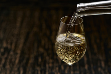 Pour white wine into a glass on black wooden background, close-up.