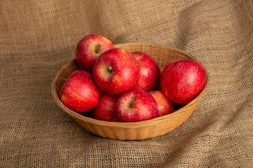 Fototapeta na wymiar Fresh red apples in basket on sack background with copy space
