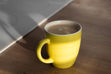 Yellow mug or cup of coffee on wooden table in the morning