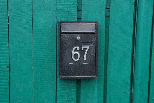 black metal mailbox with number 67 on a green wooden fence