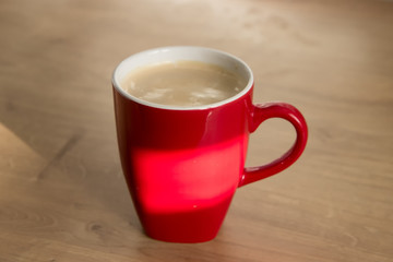 Red mug or cup of coffee on wooden table in the morning