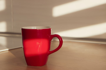 Red mug or cup of coffee on wooden table in the morning