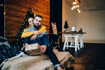 Beautiful cheerful couple sitting on bed with Christmas present