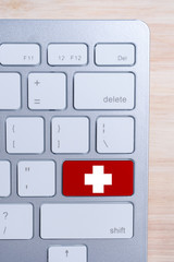 Fototapeta premium The concept of medical care online. Cross on the keyboard button. Top view. Vertical.