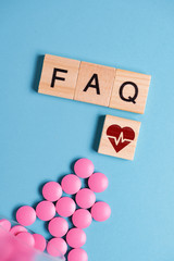 The concept of basic, general questions on medicines, pills for the heart. Pink tablets next to wooden square and letters - FAQ.