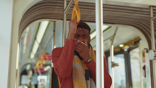 Poor ill bearded young man sneezing allergy while driving in tram. Unwell business guy in coat suffering cold or flu going to work despite illness.