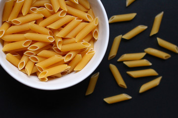 A white bowl filled with Italian penne on a dark background