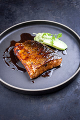 Minimalistic design Japanese salmon fish filet with avocado and wasabi creme glazed in teriyaki sauce as closeup on a modern design plate