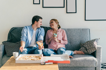 Laughing couple eating pizza on couch