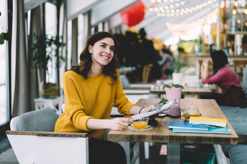 Young smiling brunette sitting while reading magazine