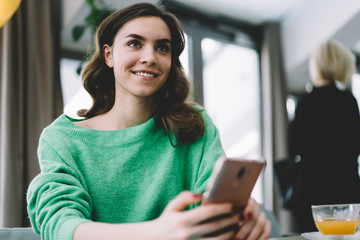 Young smiling brunette in green sweater with smartphone