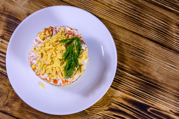 Plate with traditional russian salad Mimosa on a wooden table. Layered salad with potatoes, sardine, cheese, carrot, eggs and mayonnaise. Top view