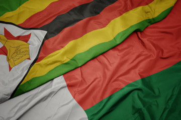 waving colorful flag of madagascar and national flag of zimbabwe.