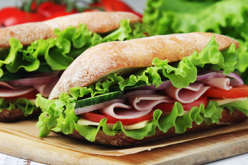 Two sandwiches with fresh vegetables, ham and cheese in ciabatta bread