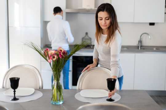 Woman Setting The Table While Her Boyfriend Is Cooking