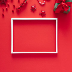 Christmas modern composition. White photo frame, Xmas decorations on red background. Christmas, New Year, winter concept. Flat lay, top view, copy space