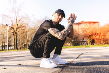 portrait of young rapper posing in the middle of an outdoor basketball court - obrazy, fototapety, plakaty