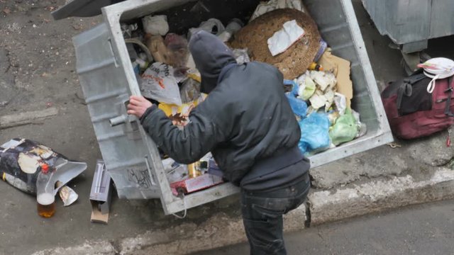 Homeless, Poor man rummaging through garbage bin in search of something to eat.
