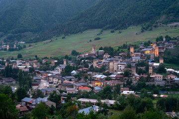 Fototapeta na wymiar Evening view on Mestia with its beautiful illuminated Svan Towers and high mountains. Svaneti, Georgia.