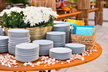 white dishes stacked basket with white flowers, outdoor buffet, white porcelain plates,  natural flowers