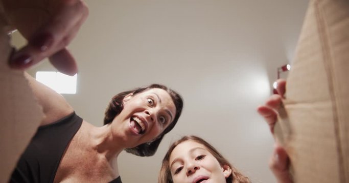 Merry Christmas and Happy Holidays! Cheerful mom and her cute daughter girl opening a Christmas present. Parent and little child having fun indoors. View from inside of the box. 4K.