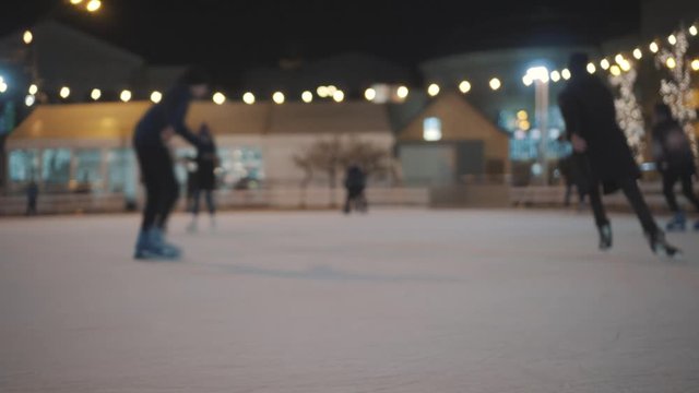 Legs of unrecognizable people ride on a city open ice rink in the evening. Winter skating public rink on Christmas Fair. People skate on the rink in Kiev, Ukraine on the contract area