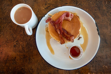A stack of American pancakes with bacon and maple syrup.