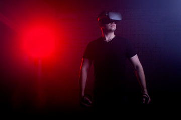 man in modern glasses of virtual reality holds wireless joysticks on a 3D background, a guy is a gamer with gaming gadgets