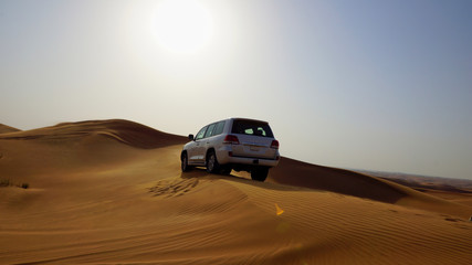Fototapeta na wymiar Off-roading: a jeep drives over large red sand dunes in the desert of the United Arab Emirates, the sunset and blue sky in the backgrpound
