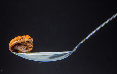 Opened walnut with exposed seeds, Juglans regia, on the tip of a spoon against a black background