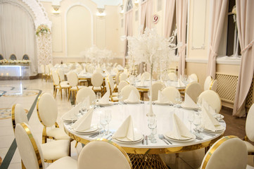 close up photo of a wedding banquet room in vintage style: arranged white round tables with golden details