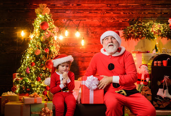 Christmas gift. Santa Claus man and little Santa boy at home. Merry Christmas. Christmas decoration. Smiling little child boy in santa costume with Santa Claus. Happy holidays. Family holiday concept.