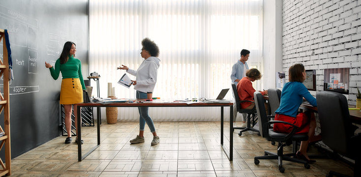 Working on a new project. Group of young multicultural people working and discussing fresh ideas in the modern office. Professional graphic designers in casual wear working together