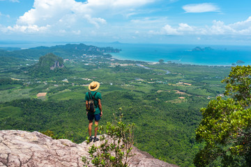 Young traveler  stands on rock high in mountains watches beautiful landscape & sea on horizon. View of Ao Nang, bay and islands from Dragon Crest at Khao Ngon Nak Nature Trail in Krabi, Thailand