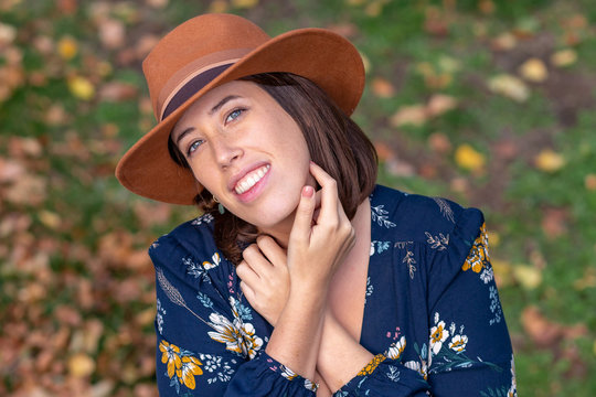 Portrait of young beautiful woman  in brown hat and blue dress in a garden with grass and leaves