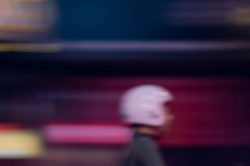 Defocused urban scene: a motorcyclist in helmet drives by along a night street, blurred in motion. Panning technique. Blurry purple urban abstract.