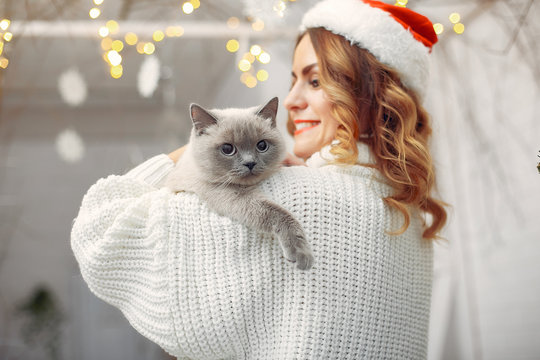 Elegant girl in a white sweater. Woman sitting by the christmas tree. Lady with little kitty