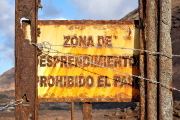 A rusty warning sign in Spanish: zona de desprendimiento prohibido el paso (English: entry prohibited, falling stones zone).