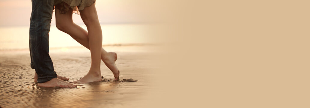 A loving young couple hugging and kissing on the beach. Lovers man and woman barefoot in the wet sand. Summer in love.